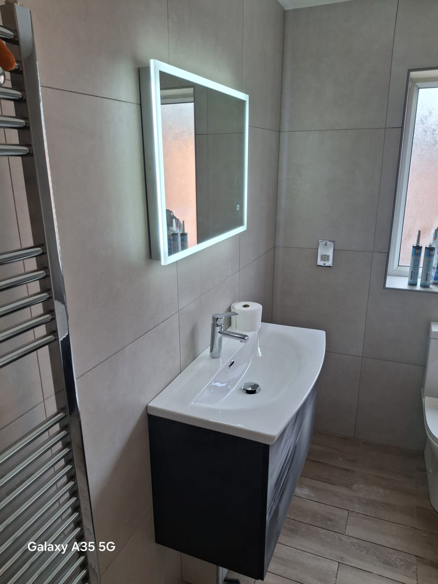 Modern grey-tiled bathroom with wall-hung black vanity, ceramic basin and LED backlit mirror