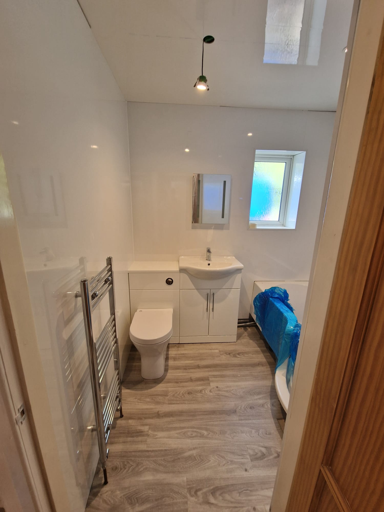Newly fitted compact white bathroom with vanity unit, WC and bath, finished in oak-effect flooring