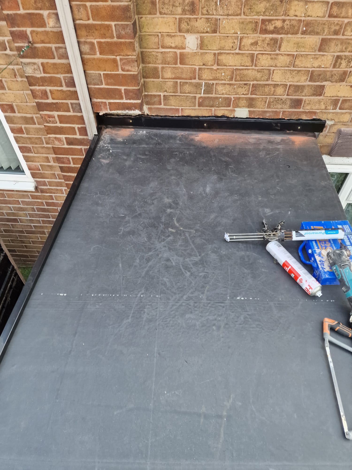 Black EPDM rubber flat roof installation in progress on a brick rear extension