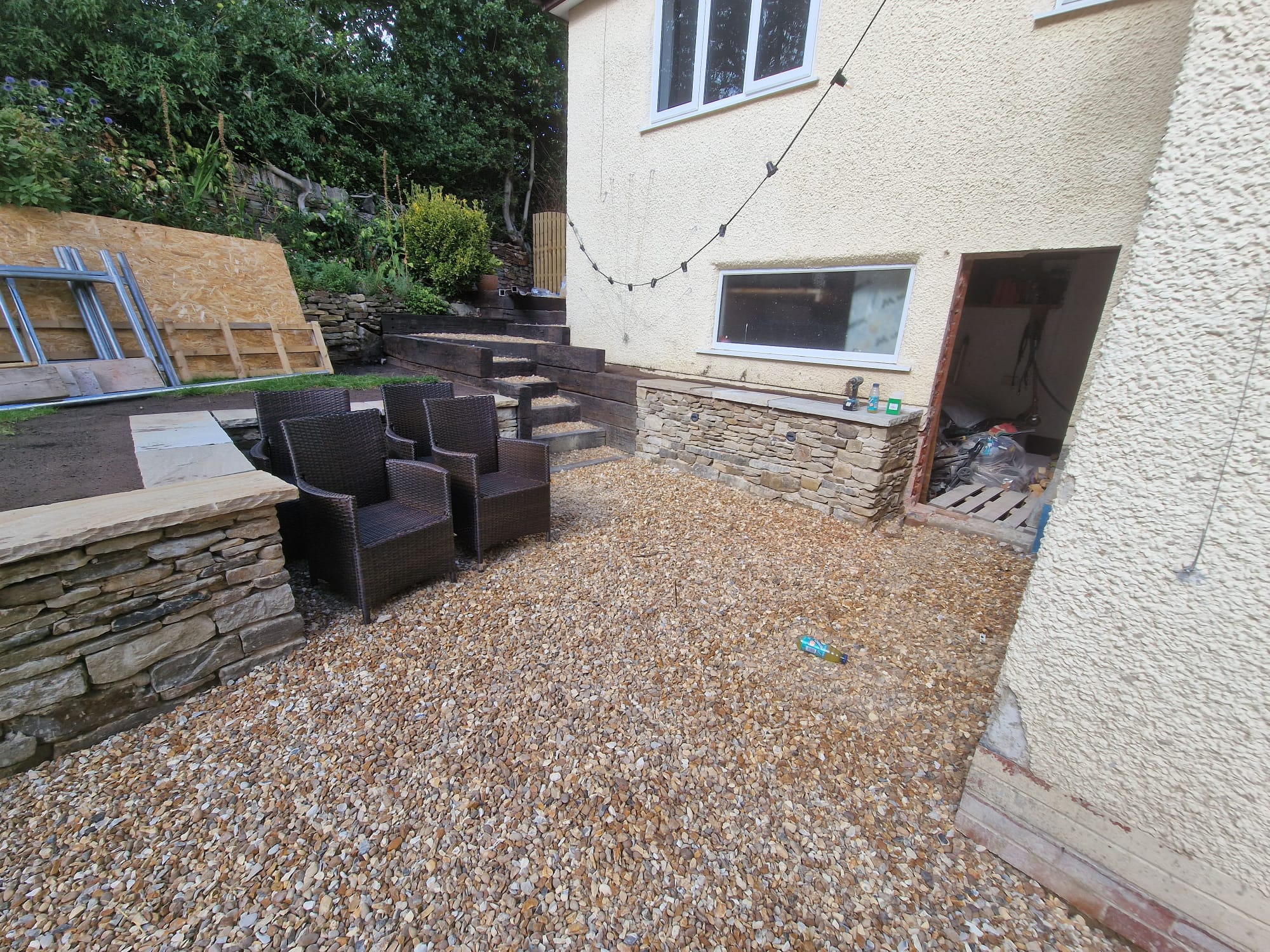 Multi-level garden courtyard with golden gravel, hand-built dry-stone retaining walls and sleeper steps