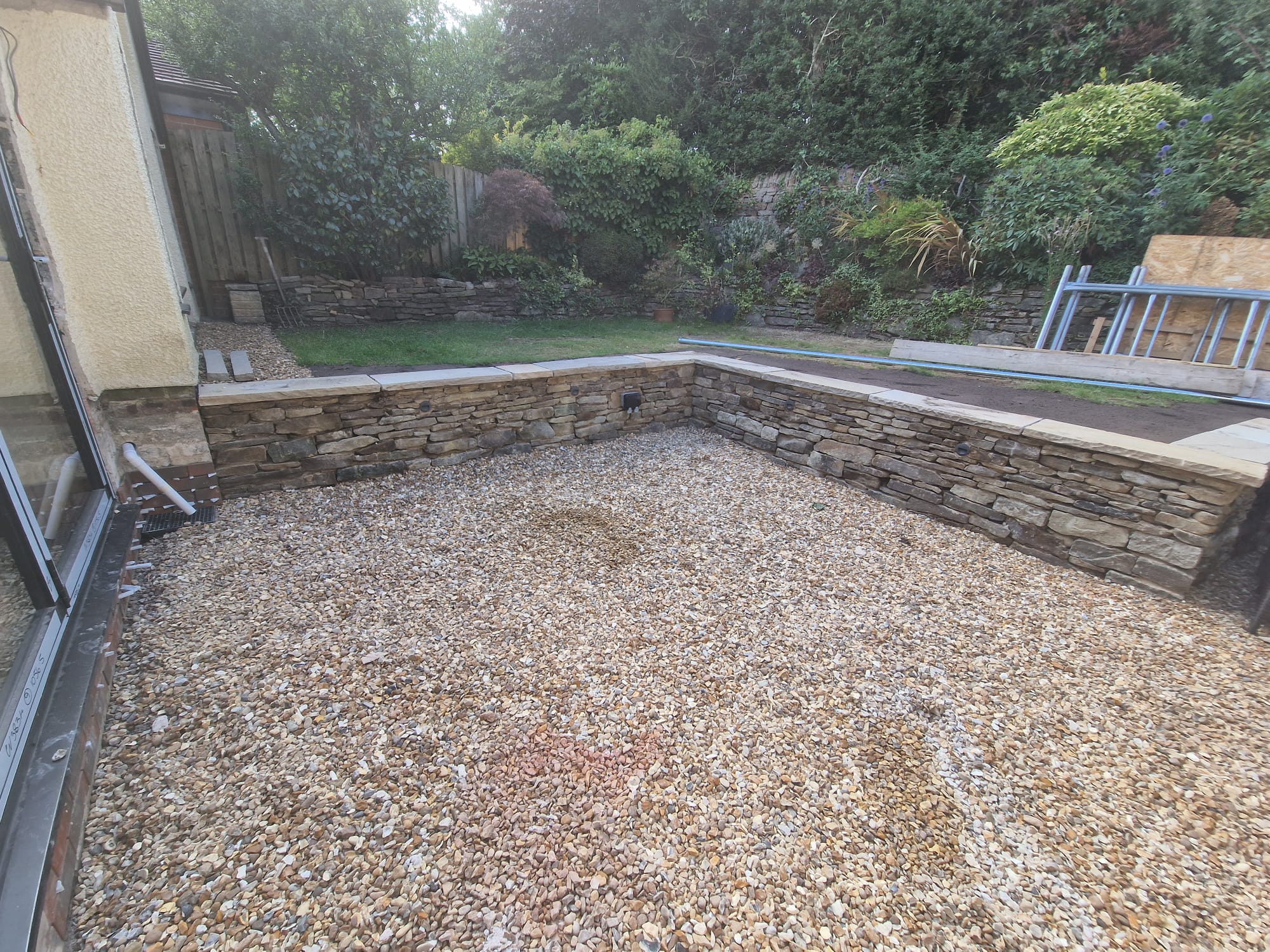 Sunken gravel garden surrounded by hand-built dry-stone retaining walls with planted upper border