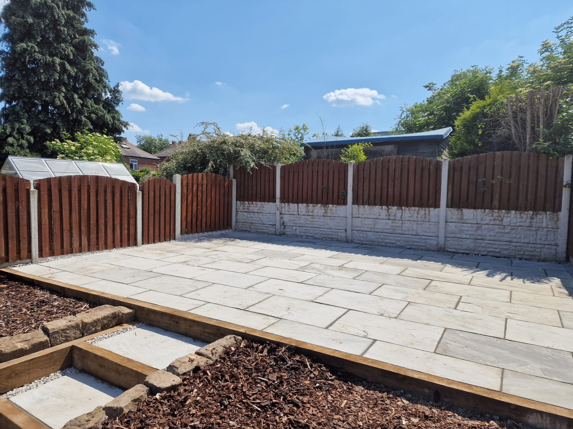 Newly laid Indian sandstone patio with timber sleeper border and stepped bark-mulched planting bed in a Yorkshire back garden